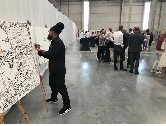 Philippe Rilos dessine une fresque en direct devant plusieurs panneaux, lors d'un événement d'entreprise
